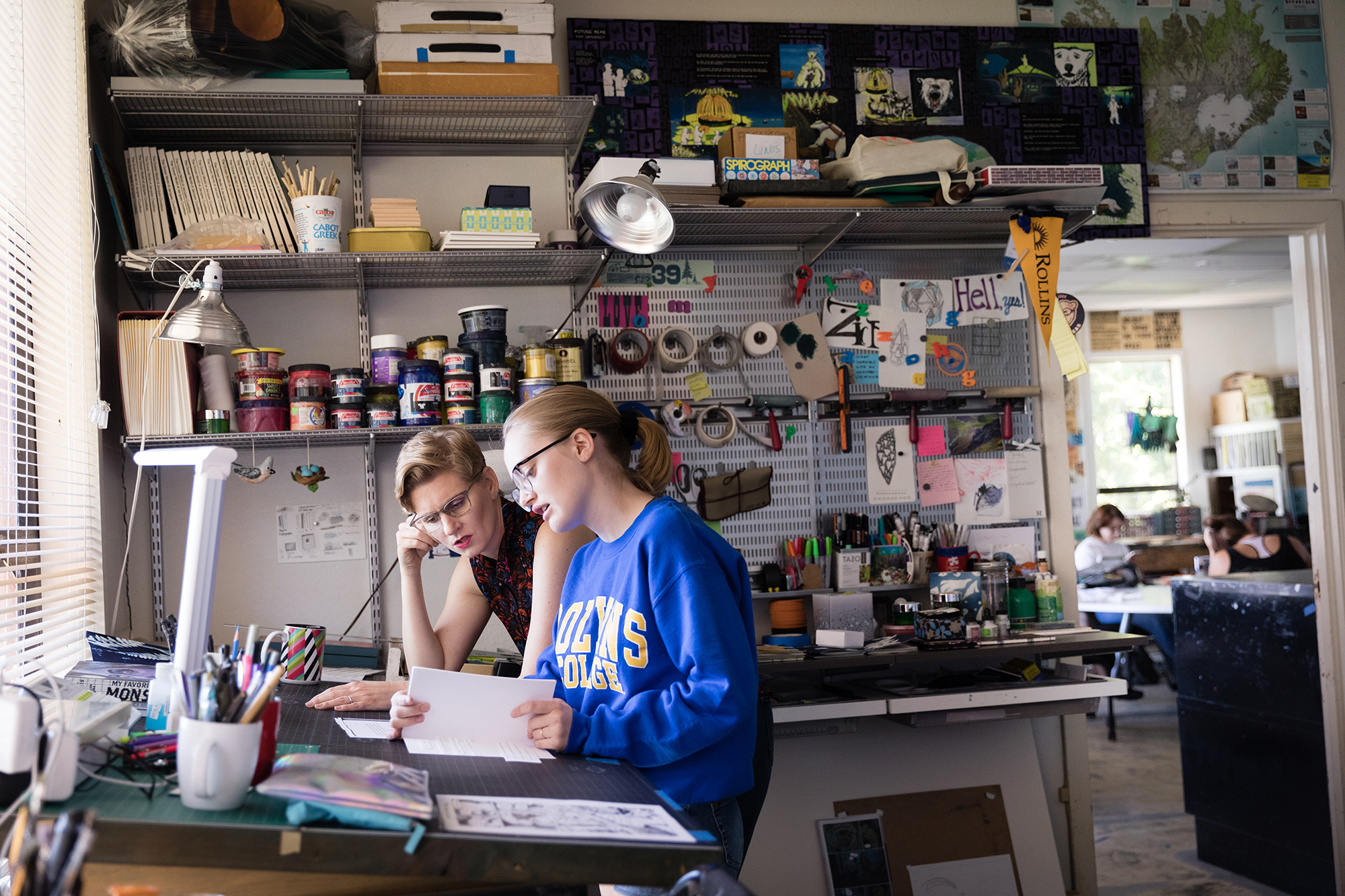 A studio art student works alongside her professor on a project.